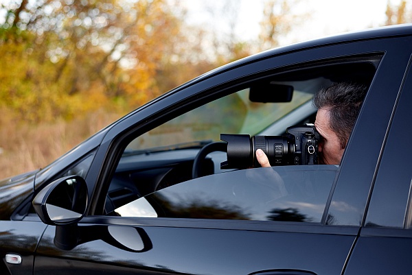 A private investigator in a car taking photos with a camera.