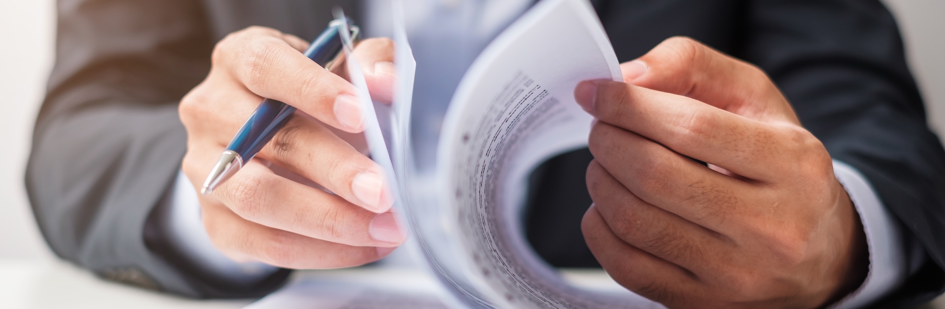 A business partner reviewing and examining contract documents with pen in hand before signing a partnership agreement.