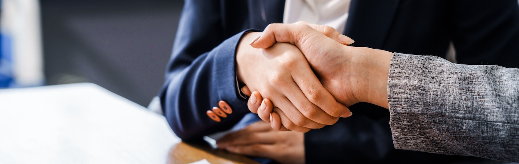 Two professional women are shaking hands in a business meeting, representing an agreement before filing a lawsuit.