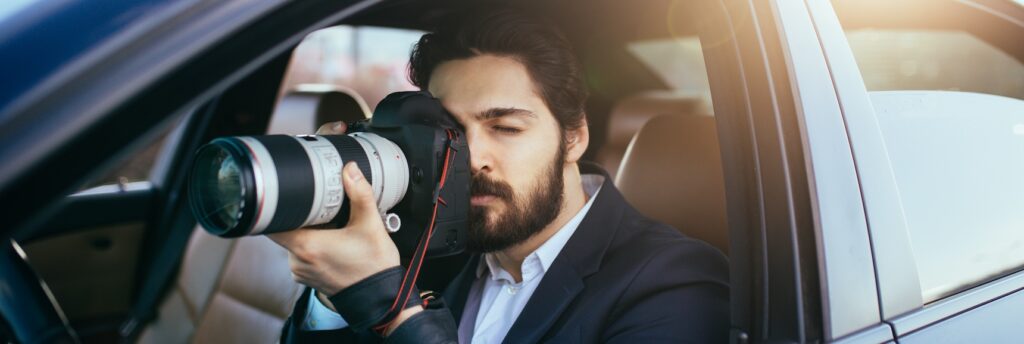 A private investigator is trying to prove an ex's cohabitation, conducting surveillance with a professional camera from inside a vehicle.