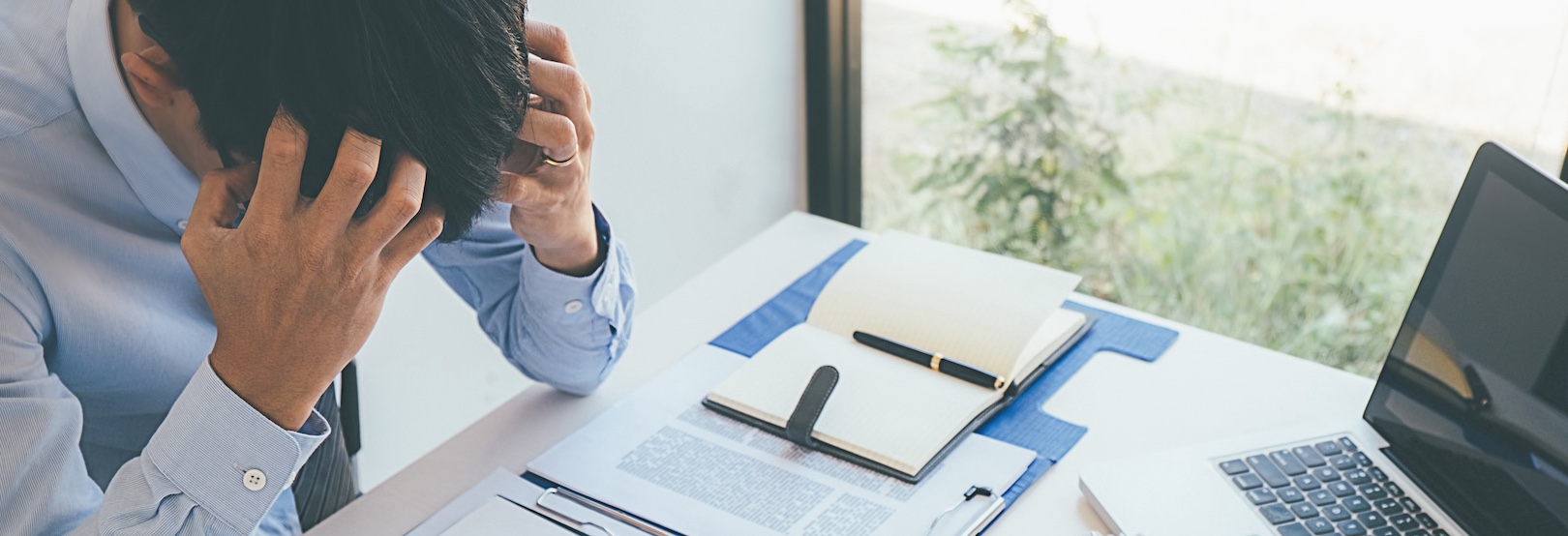 A stressed businessman with his hands on his head and is distressed after doing a background check, which revealed several concerns preventing him from signing a partnership agreement.