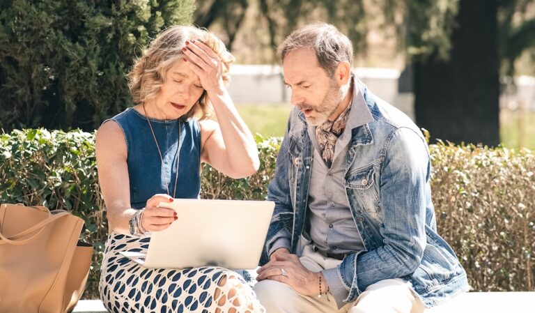 A concerned senior couple sitting on an outdoor bench, reviewing suspicious financial documents as an undercover elder investigates potential exploitation.