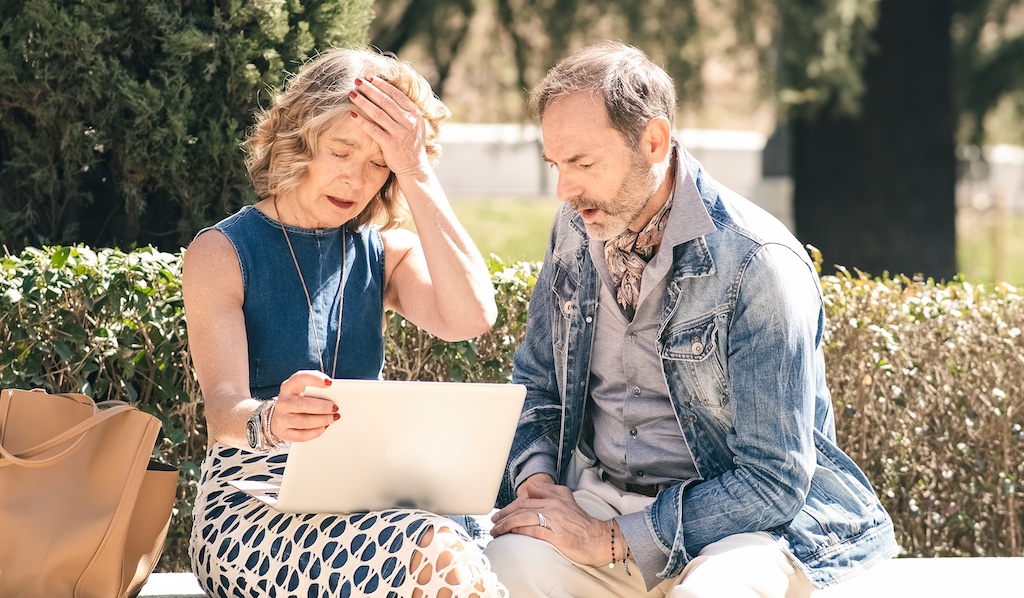 A concerned senior couple sitting on an outdoor bench, reviewing suspicious financial documents as an undercover elder investigates potential exploitation.