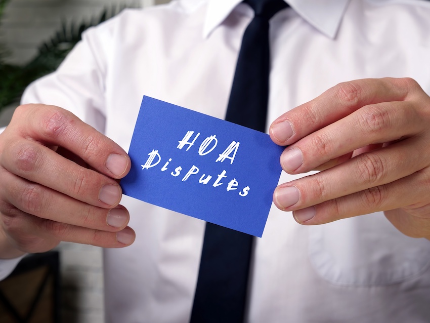 A man in a white dress shirt and tie holds up a blue card with the words 'HOA Disputes' written on it directly referencing the legal conflicts between homeowners and their associations that attorneys help resolve in South Carolina.