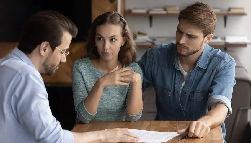 A couple sits across from an investigator at a table reviewing a document with concerned expressions illustrating the moment homeowners begin to realize they may have fallen victim to contractor fraud and are seeking legal guidance from Upstate Private Investigators.
