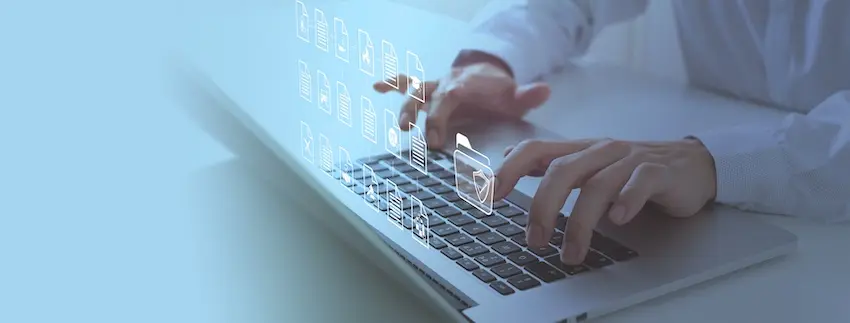 A pair of hands in a white long-sleeved shirt are shown actively typing on a silver laptop keyboard while a glowing digital overlay of multiple floating document icons- file folder symbols- and a shield emblem with a checkmark rise from the keyboard surface in a soft blue-tinted light suggesting the digital retrieval- review, and organization of records — depicting the electronic document management and case file investigation work conducted by professionals providing insurance claims support to accident victims and policyholders in the upstate of South Carolina.