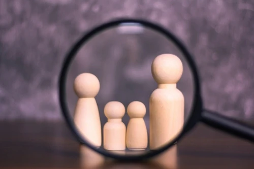 A magnifying glass and wooden dolls represent a child custody investigation.